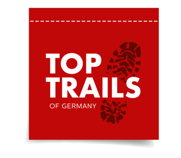 Logo TopTrails of Germany Das Logo besteht aus einem schwarzem Schuhabdruck und in weiß steht TopTrails of Germany auf rotem Hintergrund.