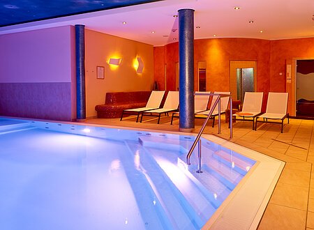 Im Vordergrund das Hallenbad mit Liegen zur Entspannung und den Wellnessbereich mit Sauna und vieles mehr im Hintergrund im Landhotel Geyer.