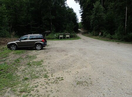 Fläche mit Schotter auf dem ein Auto parkt. Es gehen verschiedene Wege von der Fläche weg.