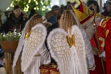 Zwei Mädchen mit Engels- und Mann im Nikolauskostüm beim Gabenverteilen
