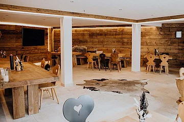 Die ländlich eingerichtete Stube ist möbliert mit massiven Holztischen, rustikalen Holzstühlen und einem Teppich aus Tierfell.