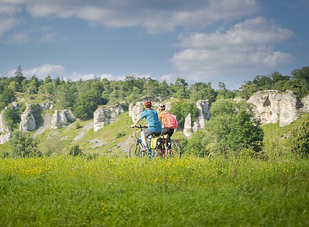 Radfahrer bei den 12 Apostel Solnhofen Zwei Personen fahren mit Fahrrädern auf einem grasbewachsenen Feld vor einer Felslandschaft.