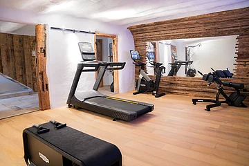 Fitnessraum mit Laufband, Fahrrad-Ergometer, Trainingsbank und großem Spiegel an der Wand.