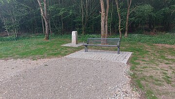 Sitzbank und Grenzstein vor bewaldeter Fläche